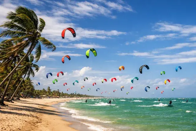 Velas de kitesurf coloridas sobre a água rasa e esverdeada de Barra Grande