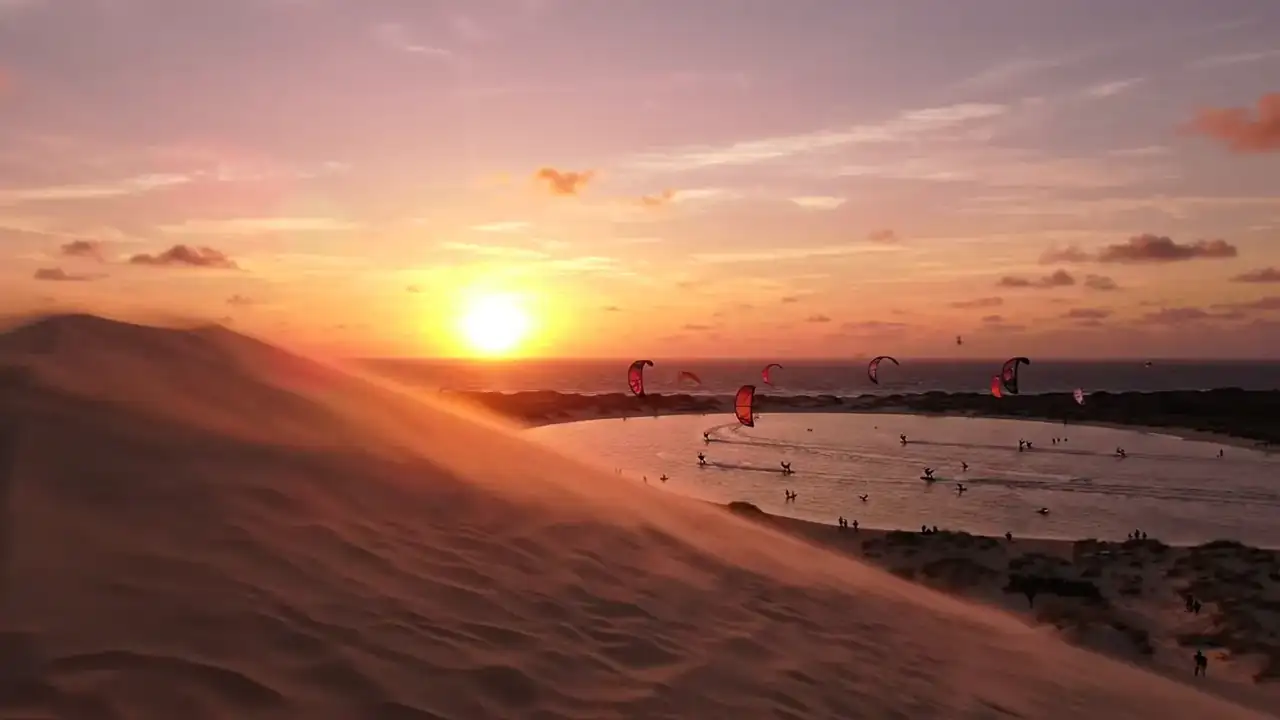 Duna de Jericoacoara ao pôr do sol com velas de kitesurf ao fundo
