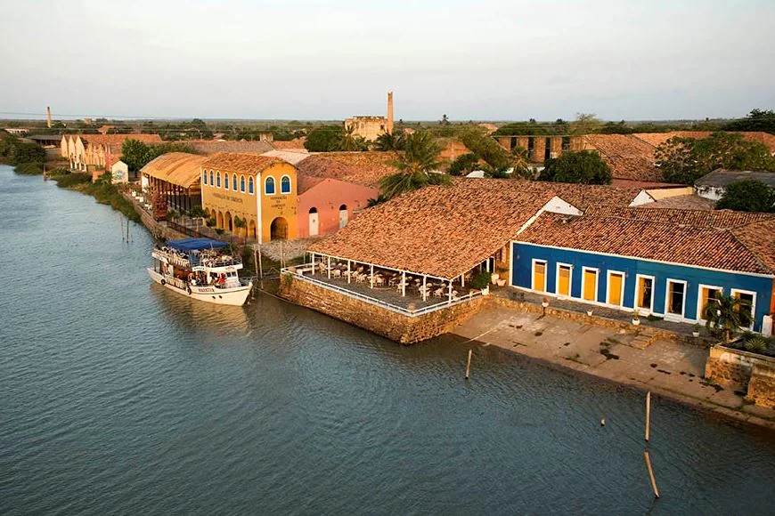 Vista aérea do Porto das Barcas em Parnaíba: os armazéns coloniais amarelos e o casario azul de telhado de barro à beira do rio Igaraçu, com um barco de passeio atracado